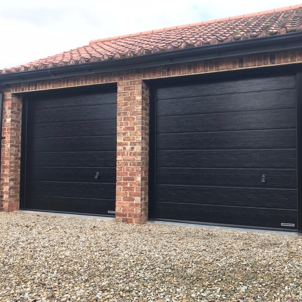 Two manually operated Hörmann  sectional garage doors finished in Black Slate Grain with an M rib panel design.